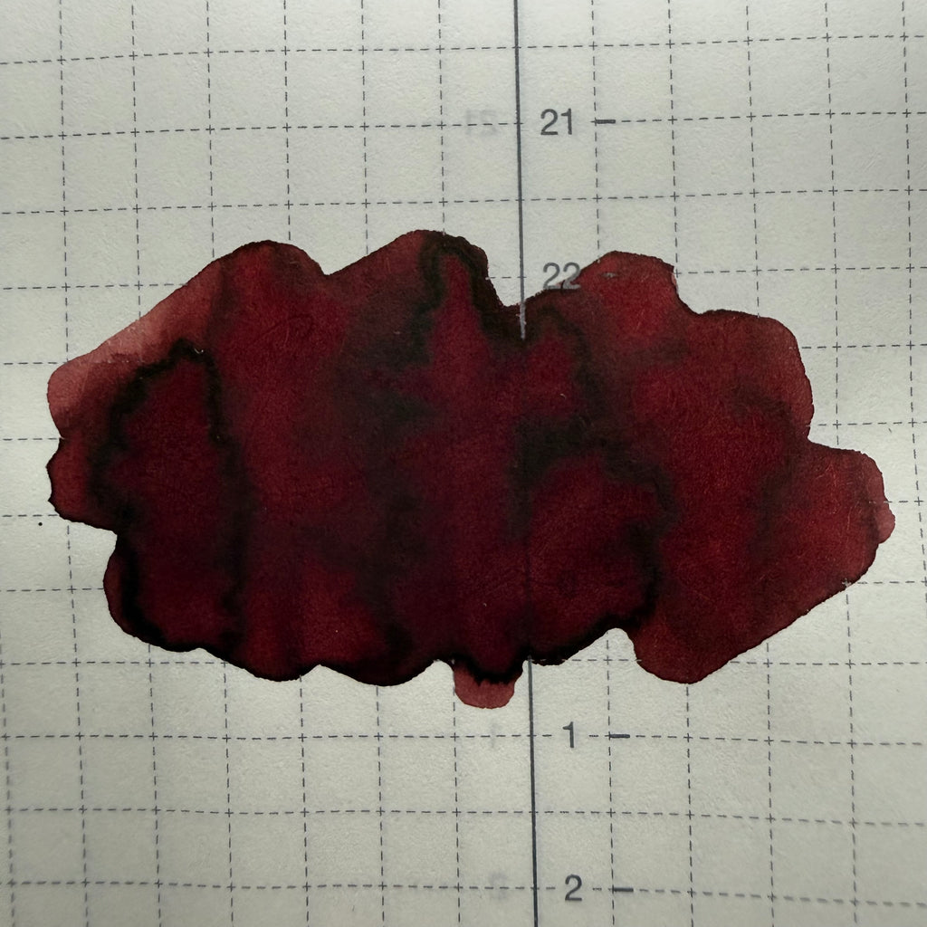 Organics Studio Edgar Allan Poe ink swatch on gridded Tomoe River 52 gsm paper, showing deep wine-red color and dark brown pooled edges
