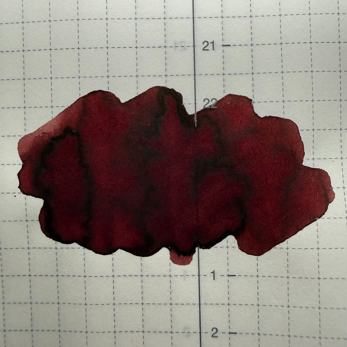 Organics Studio Edgar Allan Poe ink swatch on gridded Tomoe River 52 gsm paper, showing deep wine-red color and dark brown pooled edges