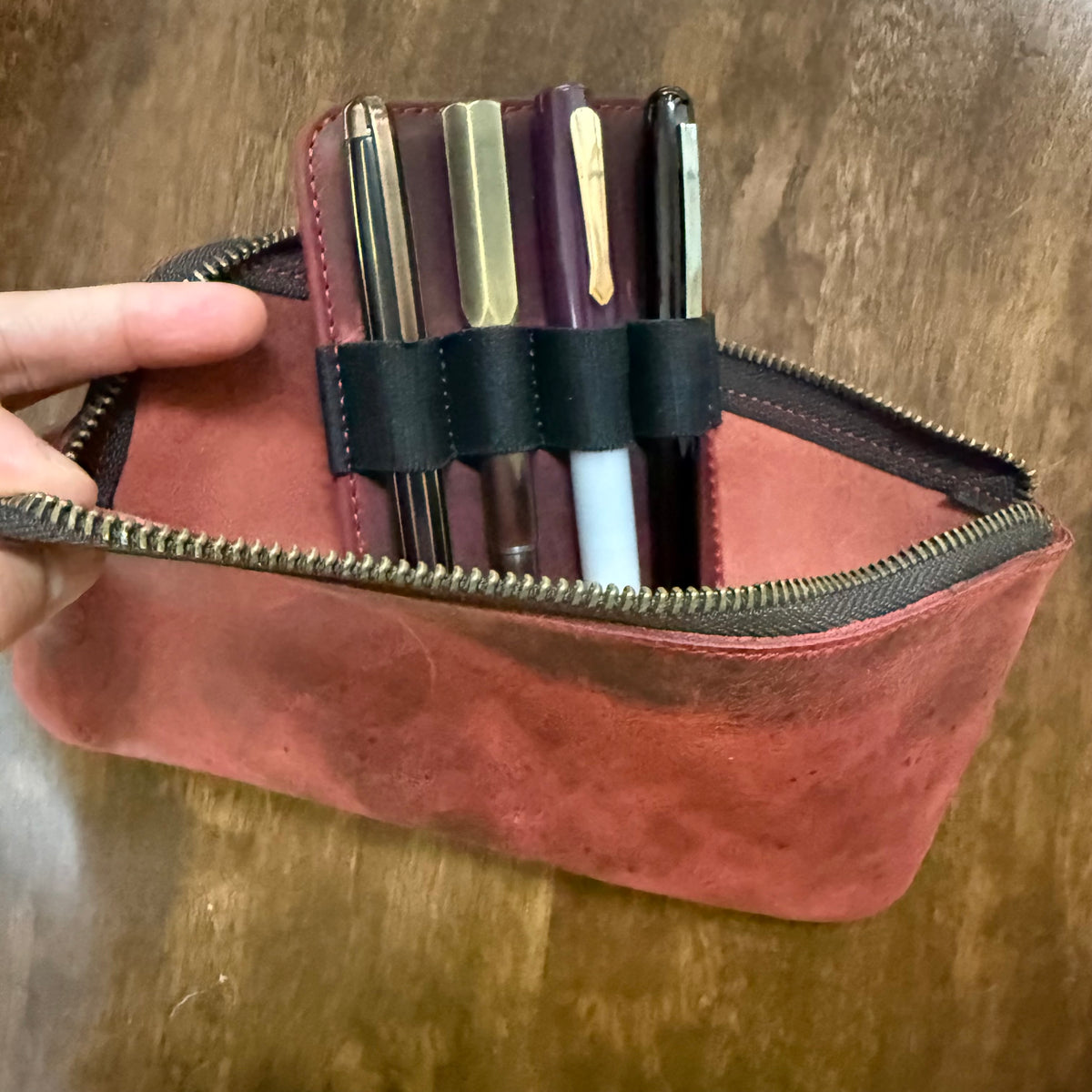 Open red cowhide leather pen case holding four fountain pens in black elastic loops