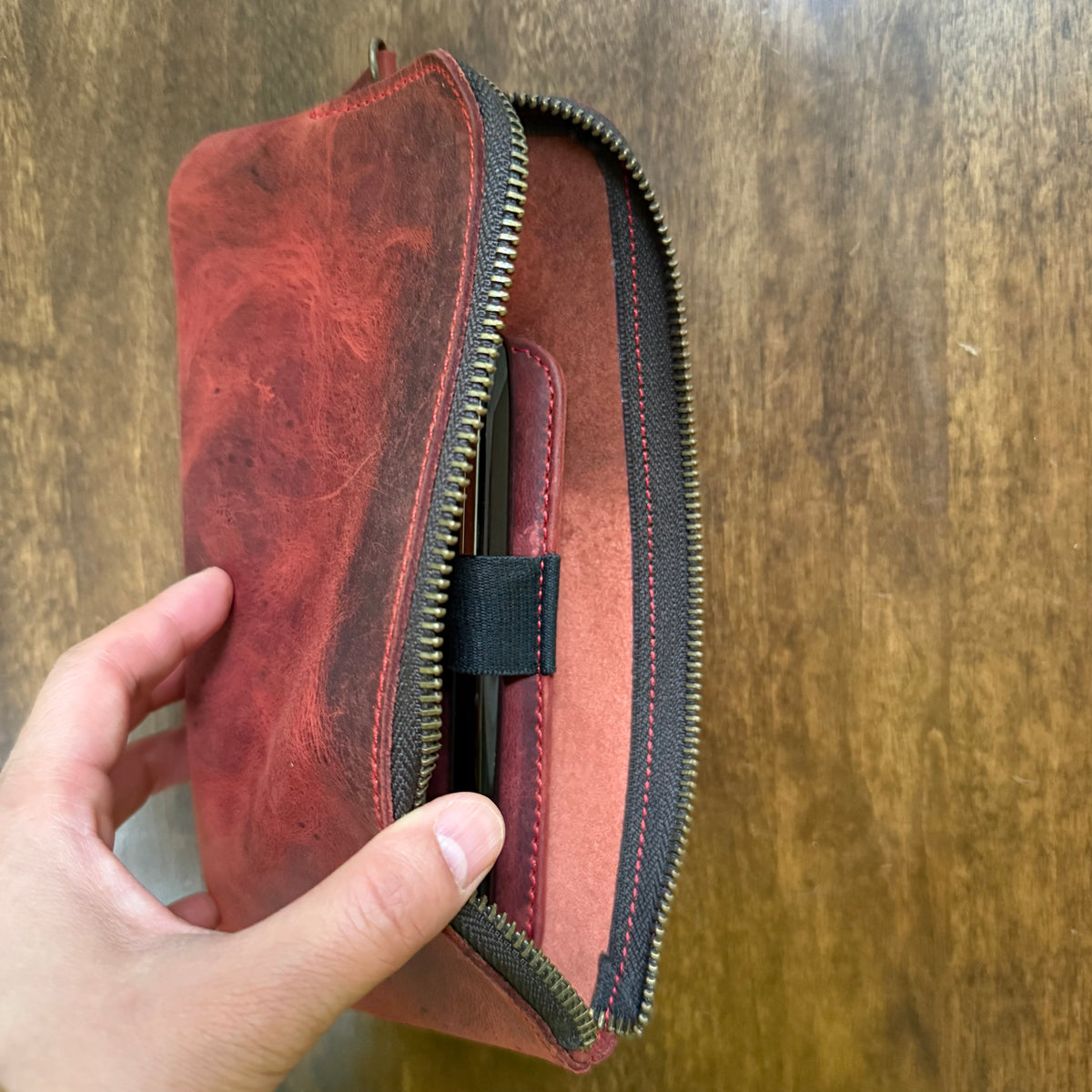 Red cowhide leather pen case being unzipped to show the interior compartment