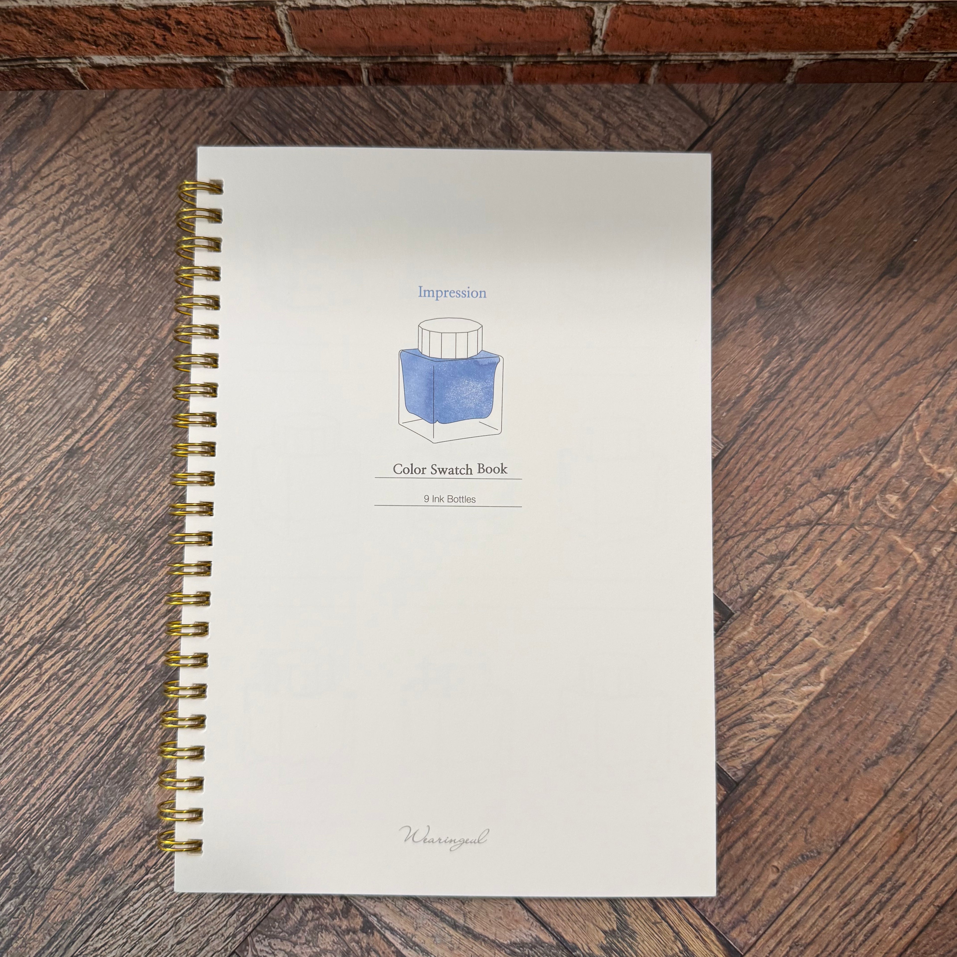 Wearingeul Impression A5 ink color swatch book with white cover, blue ink-bottle illustration, and gold-tone wire binding