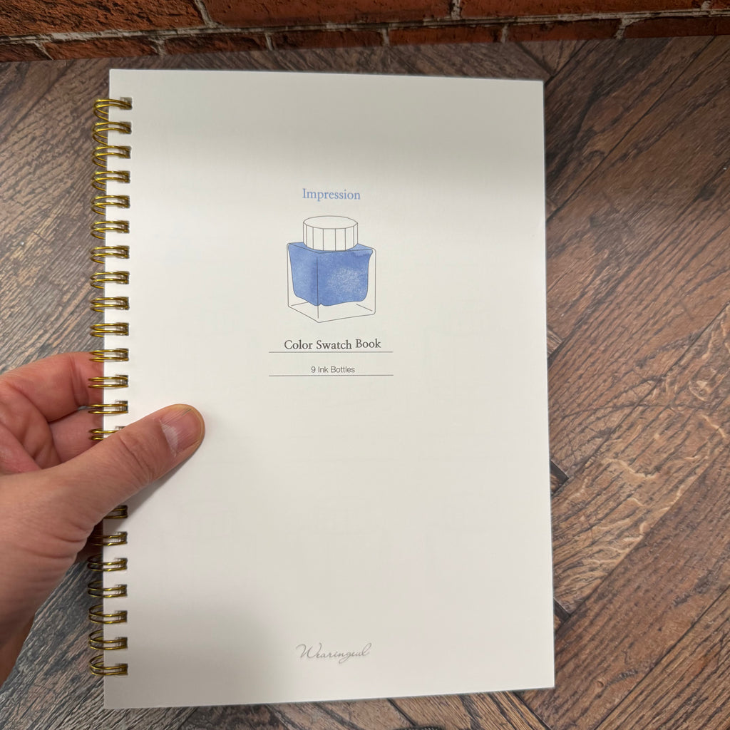 Wearingeul Impression ink color swatch book held in one hand, showing its A5 format and illustrated front cover