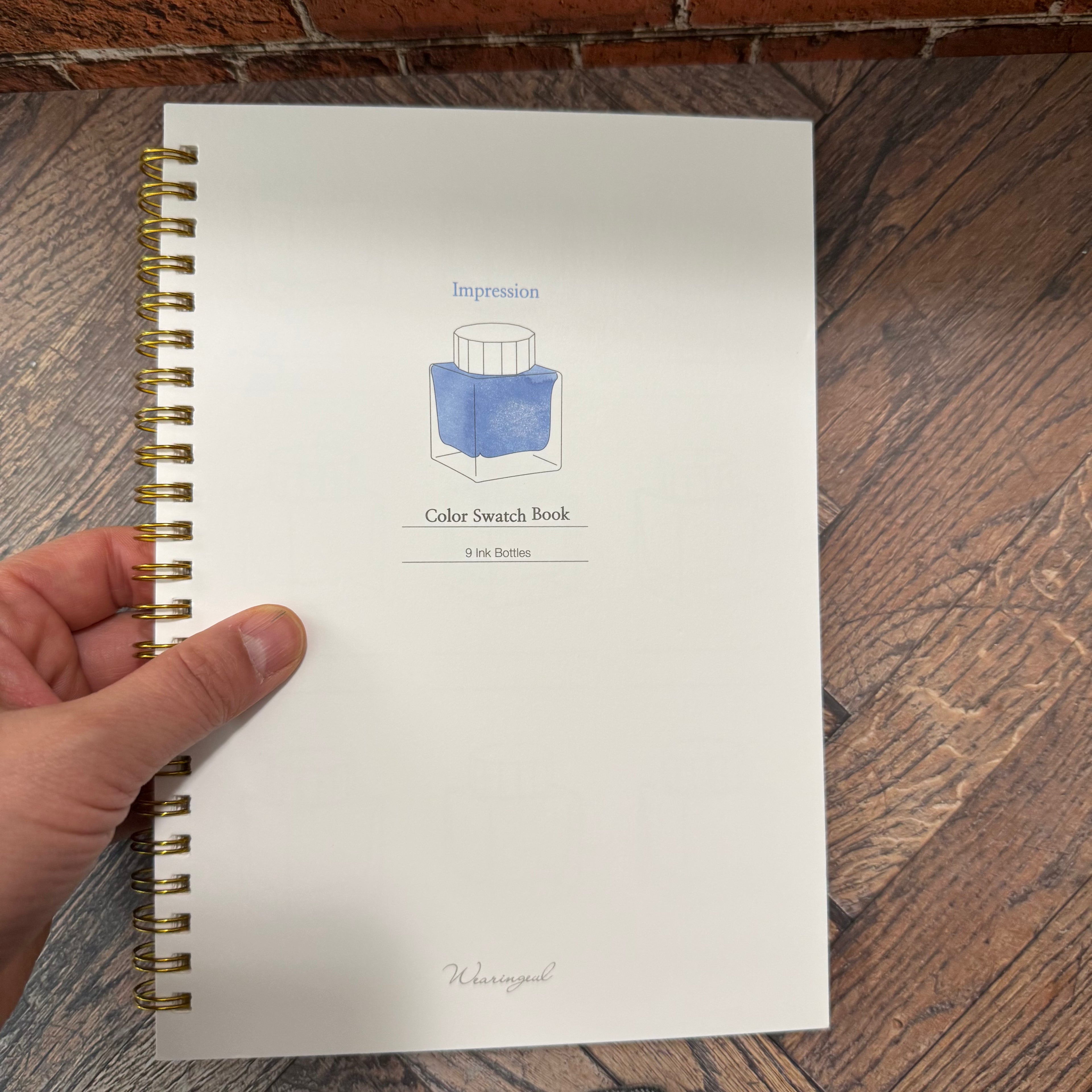 Wearingeul Impression ink color swatch book held in one hand, showing its A5 format and illustrated front cover